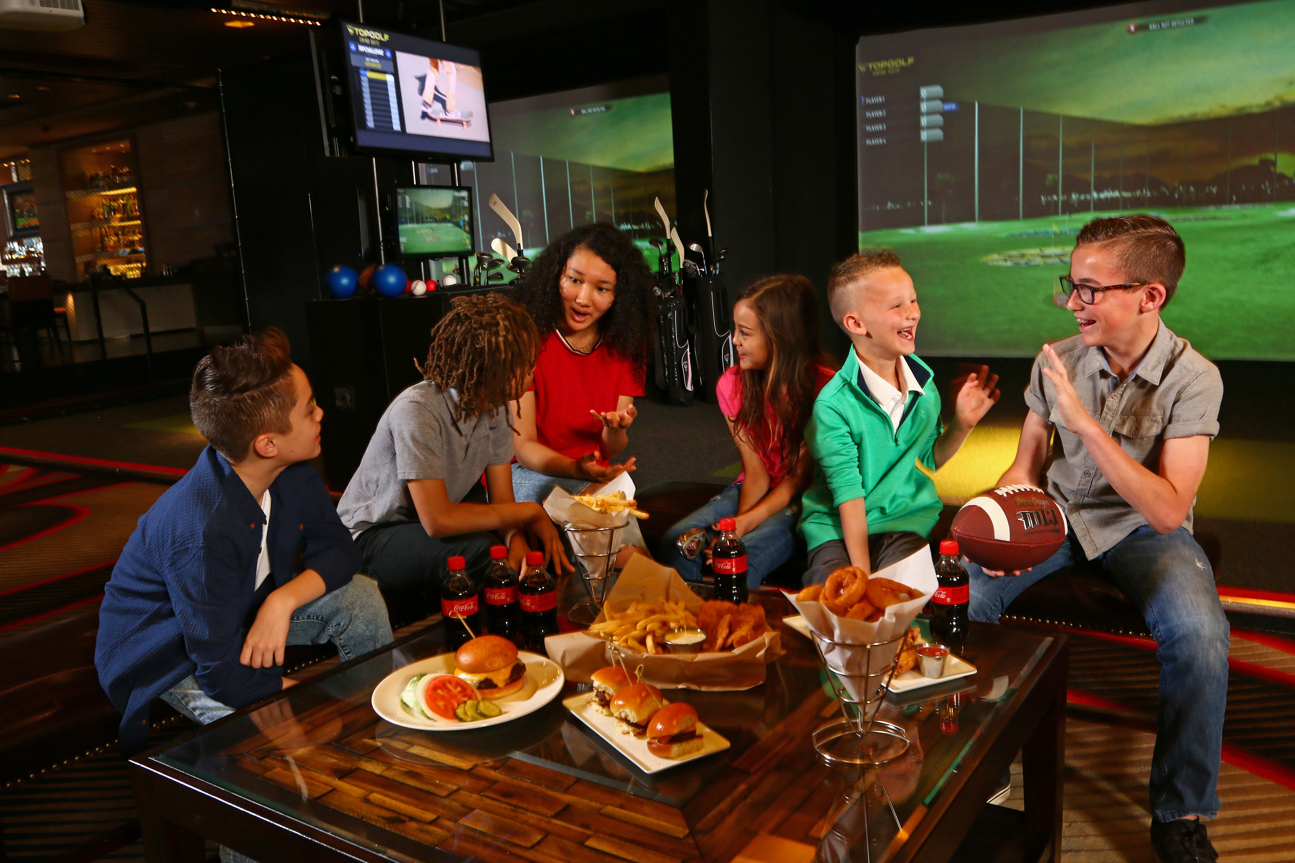 Group of kids around a table with burgers, fries, and onion rings inside the Swing Suite