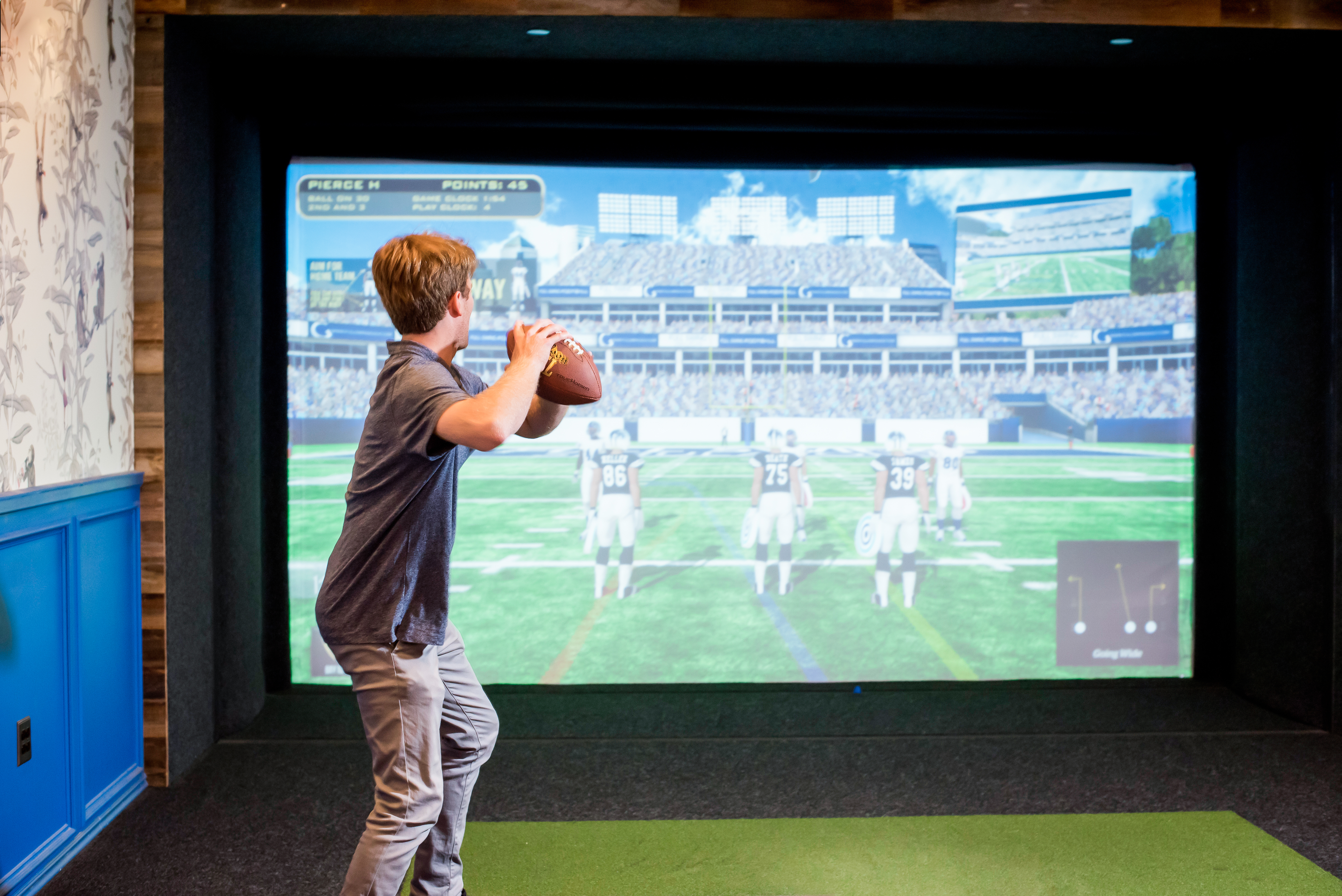 Player throwing a football at the simulator screen showing a stadium scene during a football game in the Topgolf Swing Suite