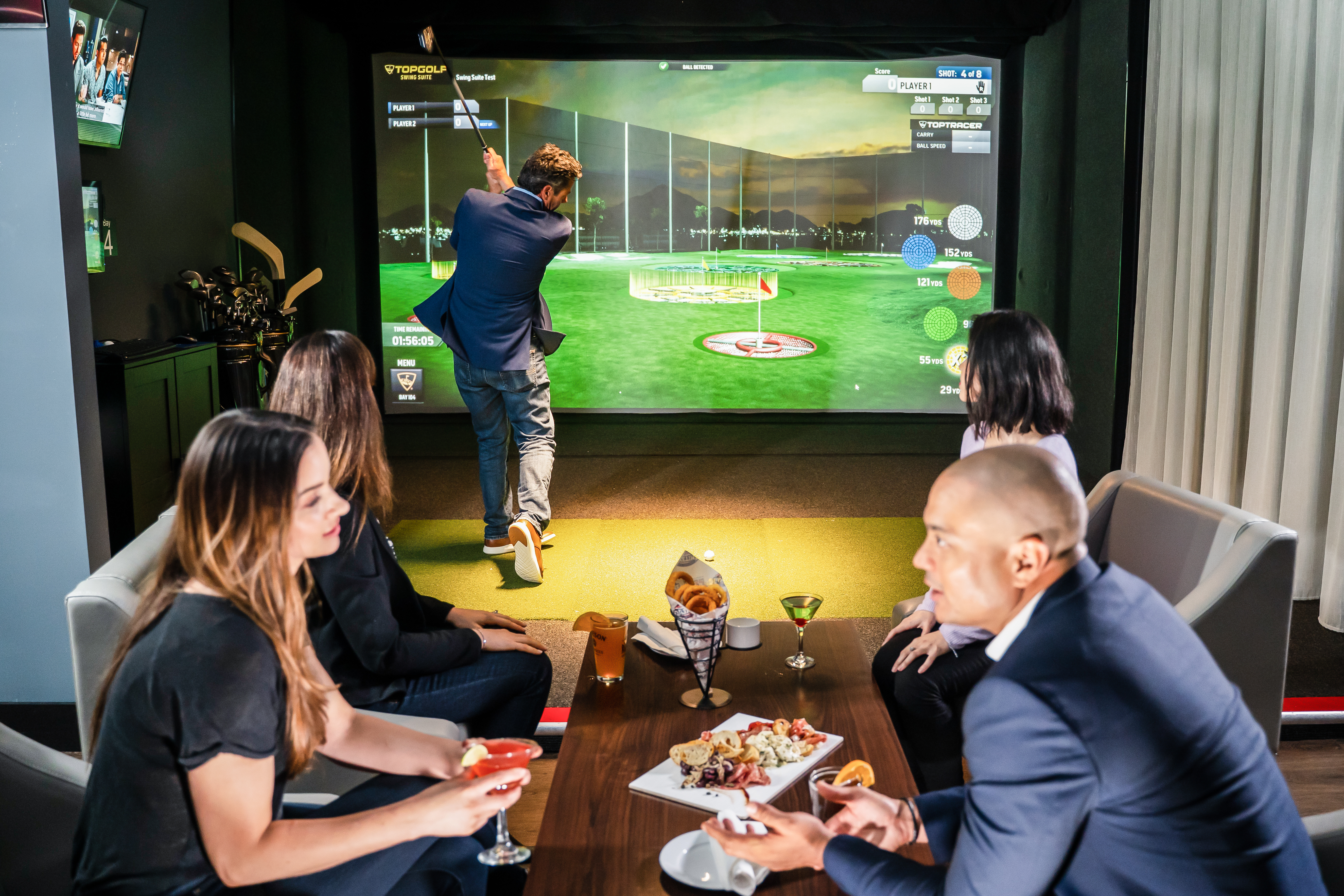 Group of guests playing the Topgolf Swing Suite at Hyatt Place Munster while enjoying drinks and food in the bay